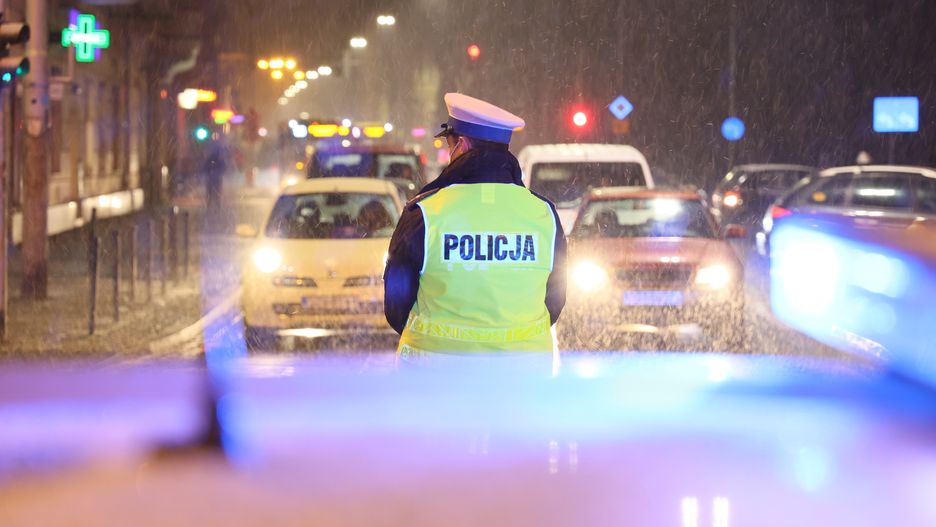 drogówka, polska, policja, zima, wieczór, noc, zimno, mróz, pada, sypie, szron, mandat, kara, kontrola, ruch, drogowy, policjant, policjantka, funkcjonariusz, ruch drogowy, wieczorem, ulica, lampy samochodów, kamizelka, odblaski, niebiescy, niebiesko, bulaje, mroźnie, alarmowo, droga, radiowóz, miejski, blur