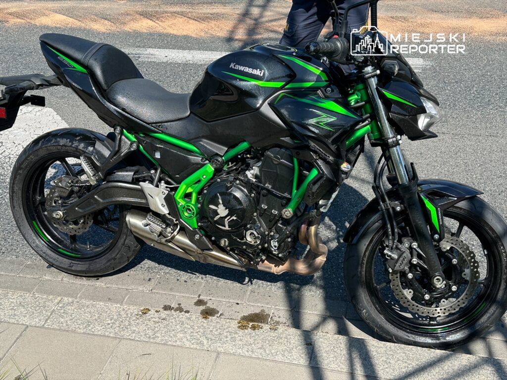 Motocykl marki Kawasaki w czarno-zielonym kolorze zaparkowany na chodniku obok ulicy.