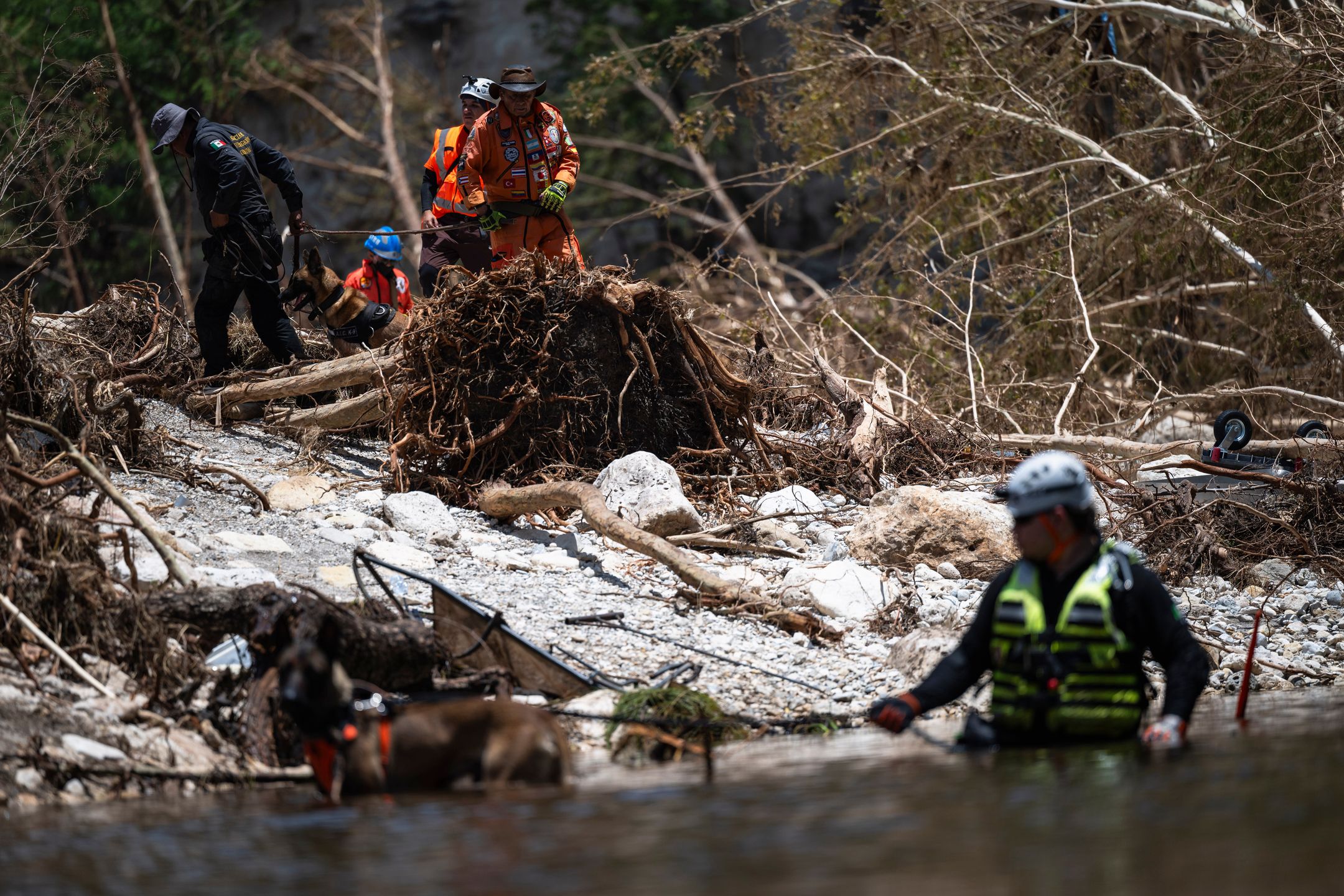 A group of volunteer rescuers from Mexico comb through flood debris with Mexican State Police and firefighters outside of Camp Mystic in Hunt, Texas, US, on Thursday, July 10, 2025. Crews in central Texas are digging through massive piles of debris, overturned vehicles and shattered homes as the search continues for victims of flash floods that killed more than 100 people over the Fourth of July weekend. Photographer: Eli Hartman/Bloomberg via Getty Images