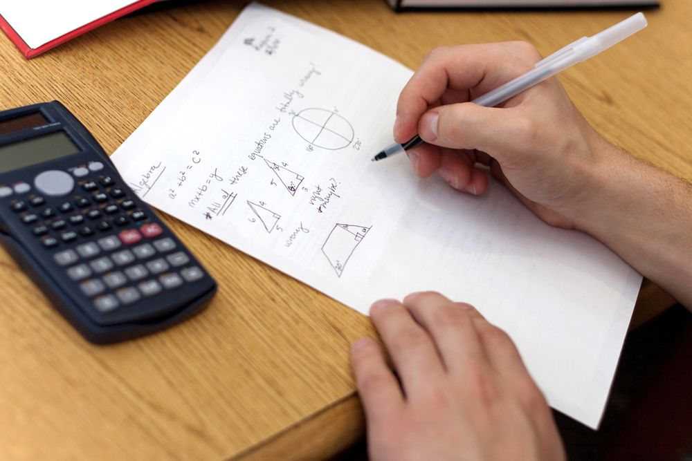 Zdjęcie A young man working out mathematical equations on paper. pochodzi z serwisu Shutterstock