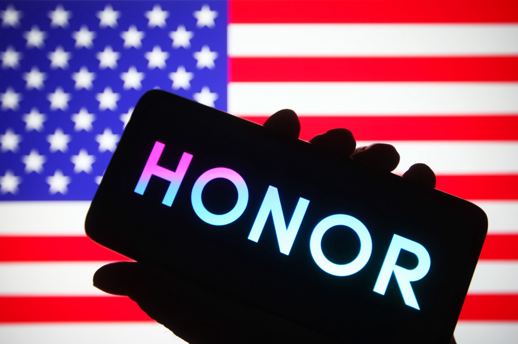 UKRAINE - 2021/10/16: In this photo illustration, HONOR logo is seen on a smartphone in a hand in front of the US flag in the background. (Photo Illustration by Pavlo Gonchar/SOPA Images/LightRocket via Getty Images)