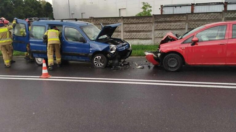 Ratownicy medyczni udzielają pomocy poszkodowanym w wypadku drogowym na ruchliwej ulicy obok dużego magazynu.