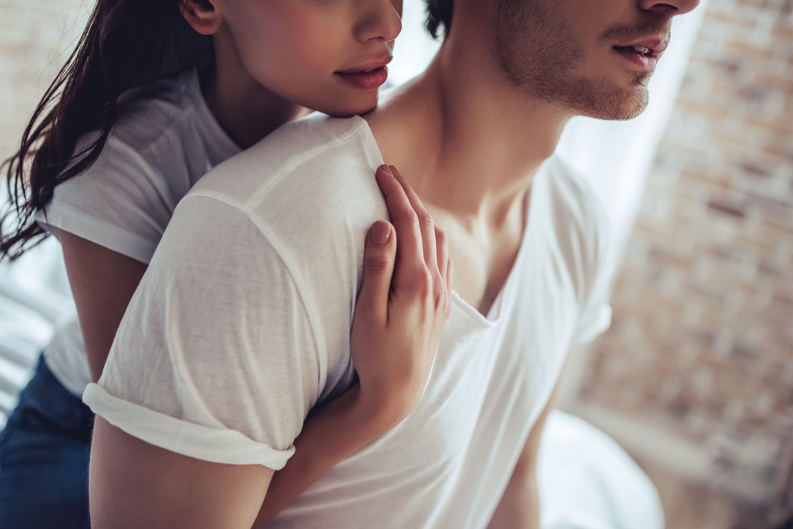 Cropped image of beautiful young couple is sitting on bed in bedroom. Enjoying spending time together at home.
