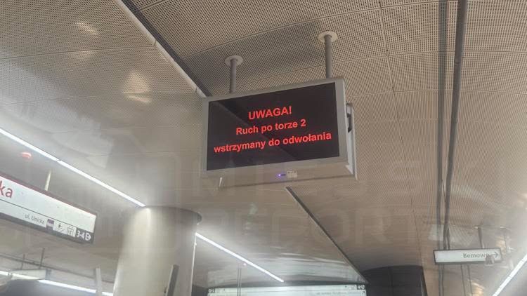 Pasażerowie na stacji metra czekają obok wyświetlacza z komunikatem: "UWAGA! Ruch po torze 2 wstrzymany do odwołania".
