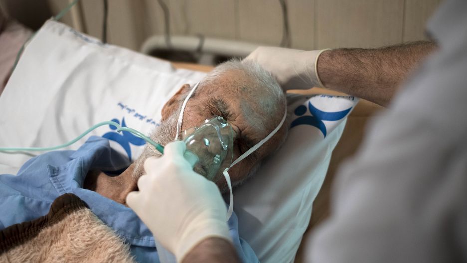 An Iranian nurse wearing a protective suit helps a patient to use oxygen at a COVID-19 ward in a hospital in the holy city of Qom 145Km (90 miles) south of Tehran amid the Omicron variant outbreak of the COVID-19 in Iran, March 10, 2022. (Photo by Morteza Nikoubazl/NurPhoto via Getty Images)