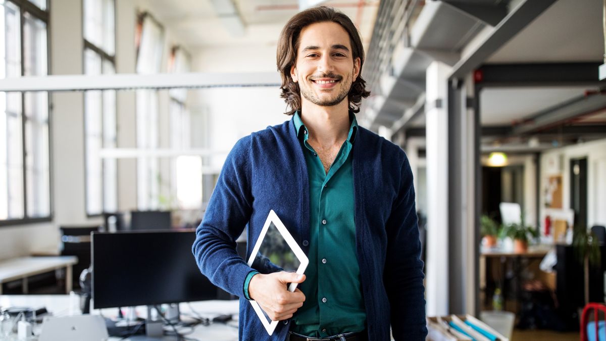 Smiling businessman standing with digital tabletPortrait of smiling young handsome businessman standing with digital tablet at creative officeLuis Alvarez