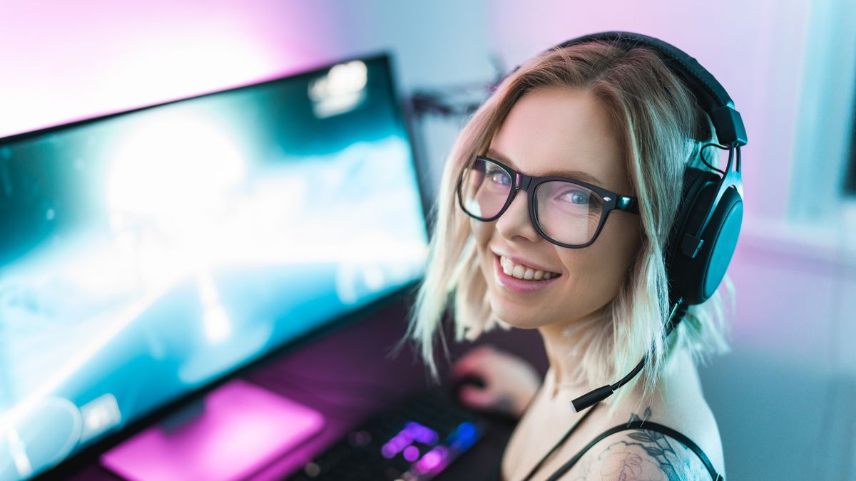 A female gamer and streamer is playing video games on her computer. Portrait of her sitting in front of her computer setup.