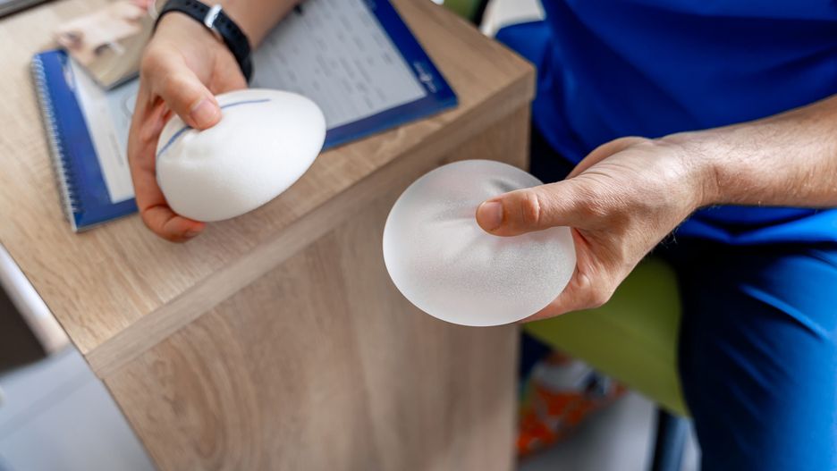 Plastic surgeon man is holding different size silicon breast implants in clinic room interior. Plastic surgery concept.Plastic surgeon man is holding different size silicon breast implants in clinic room interior. Plastic surgery concept.breast, surgery, plastic, surgeon, size, room, interior, health, medicine, doctor, nurse, treatment, shape, practice, specialist, clinic, uniform, beauty, implant, hospital, surgical, table, profession, occupation, white, medicament, medical, mask, laboratory, silicone, operation, healthcare, health-care, heal, lab, bust, anatomy, procedure, medic, physician, care, technology, practitioner, operating