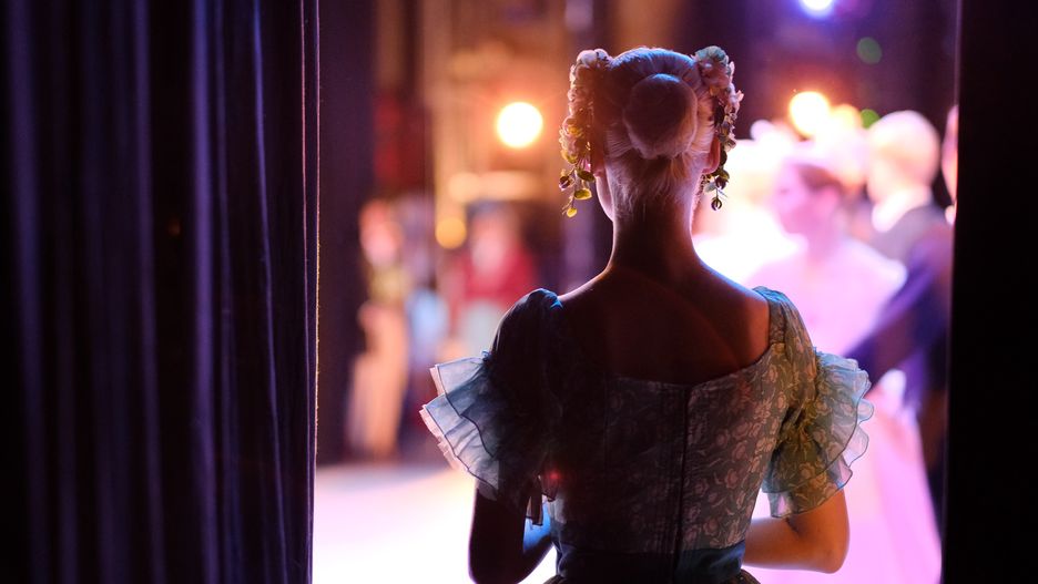 A ballerina awaiting the moment of entering the stage in the playBallet, performance, theater, stage, backstage, ballerina, premiere, training, rehearsal, art, dance, costume, dress, makeup, actor, dancer, light, illumination, background, blurred, indoors, figure, body, gesture, hairdo, Decoration, scenery, curtain, spotlights, fabric, neck, bend, posture, skill, talent, flowers, hands, position, Props, silhouette