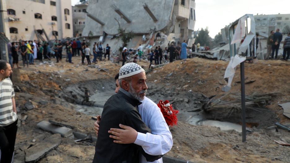 Palestinian Muslim men exchange Eid al-Fitr holiday wishes in front of a destroyed building in the northern Gaza Strip town of Beit Lahia, on May 13, 2021, the first day of Eid, which marks the end of the holy fasting month of Ramadan. - Israel's air force said it had launched multiple strikes overnight, targeting what it described as locations of Hamas, the Islamist group that controls Gaza. Meanwhile, incoming passenger planes scheduled to land at Israel's Ben Gurion airport near Tel Aviv were being diverted on May 13 to a southern airport amid rocket fire from Gaza, the airports authority said.  (Photo by Majdi Fathi/NurPhoto via Getty Images)