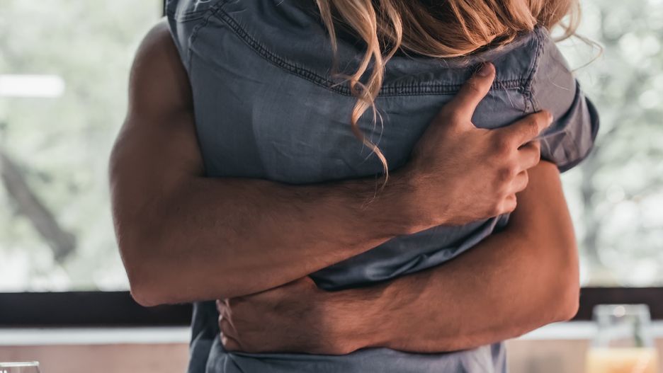 Cropped image of attractive passionate couple on kitchen. Man hugs woman while she's sitting on table.