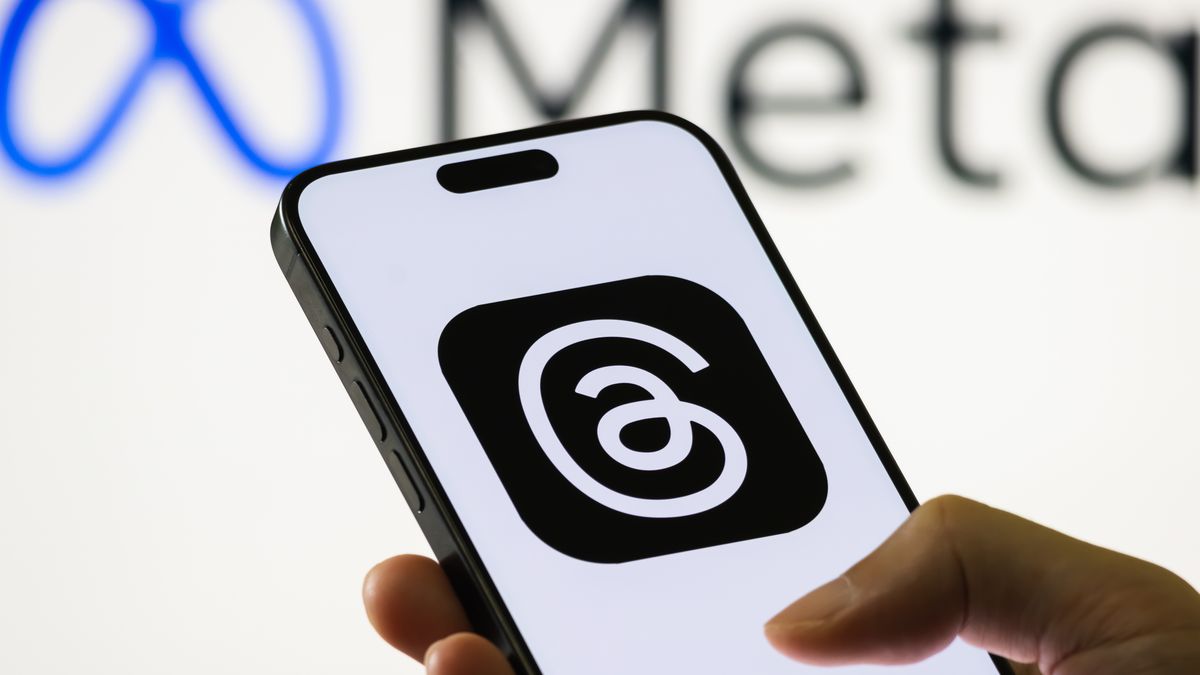 CHONGQING, CHINA - AUGUST 14: In this photo illustration, a person holds a smartphone displaying the logo of Threads, a text-based social media and microblogging app developed by Meta Platforms, with the Meta logo visible in the background, on August 14, 2025 in Chongqing, China. Threads is positioned as a companion to Instagram and a competitor to X (formerly Twitter). (Photo illustration by Cheng Xin/Getty Images)