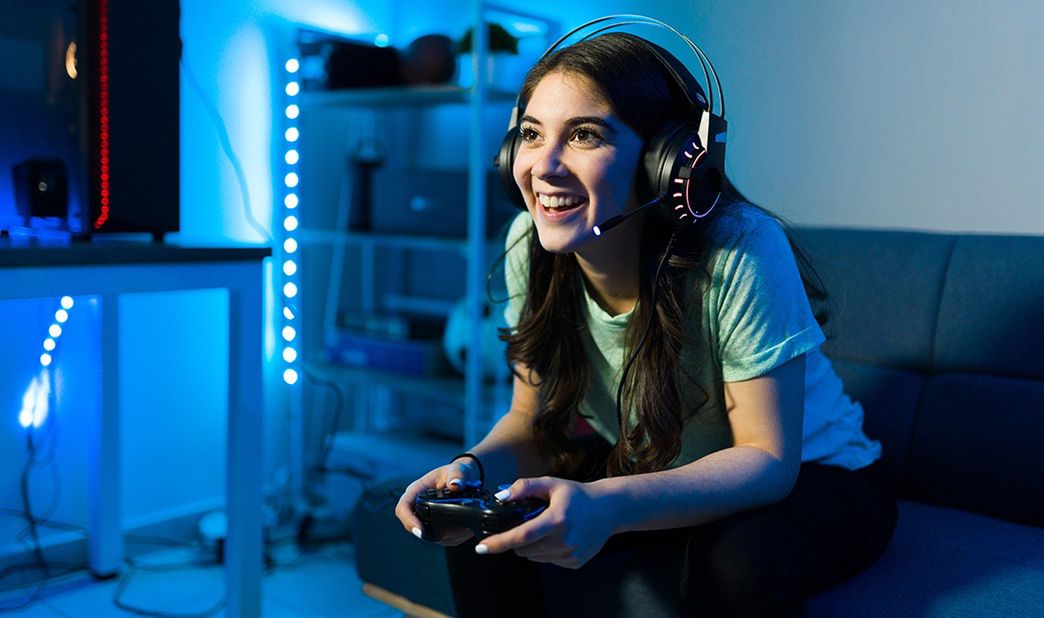 Dziewczyna w słuchawkach gra na konsoli, trzymając kontroler i siedząc na kanapie. 