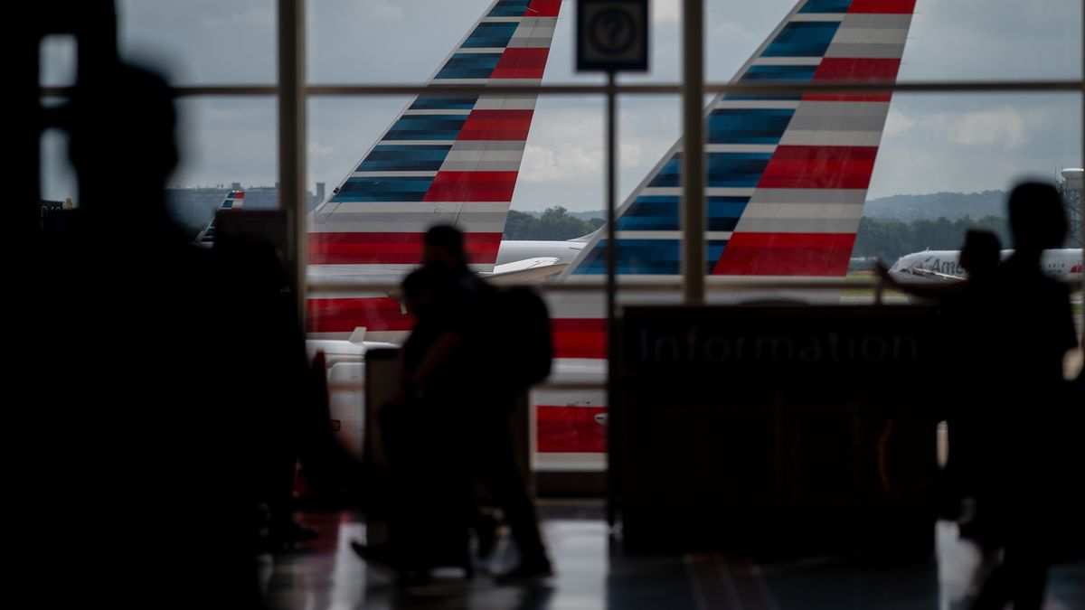 Travelers walk past American Airlines planes at Ronald Reagan Washington National Airport (DCA) in Arlington, Virginia, US, on Saturday, July 19, 2025. American Airlines Group Inc. scaled back its earnings outlook amid a persistent slump in consumer demand, casting doubt on a recovery in US travel and sending its shares tumbling. Photographer: Stefani Reynolds/Bloomberg via Getty Images