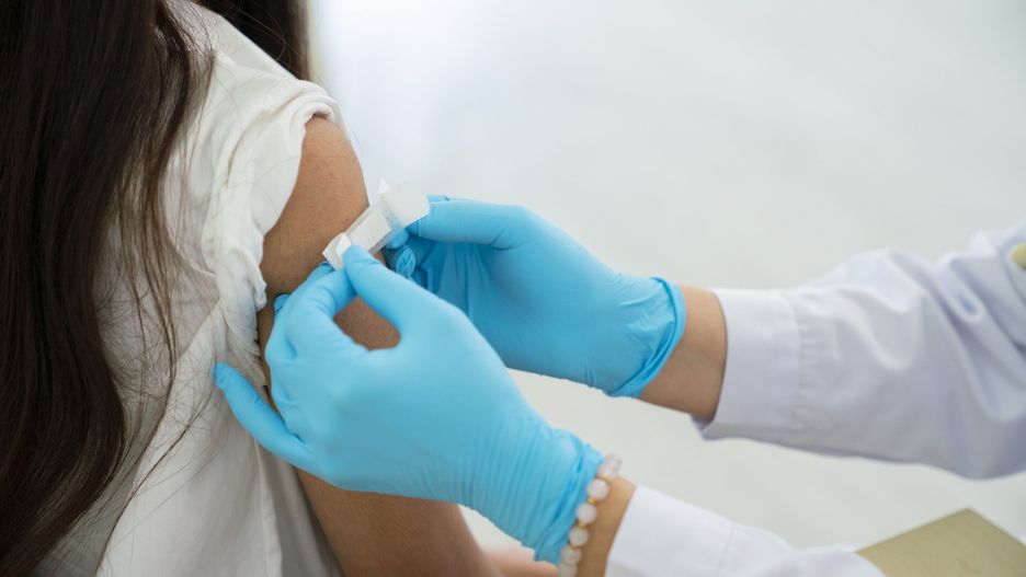 Doctor applies bandage to preteen girl&#39;s arm following an immunization