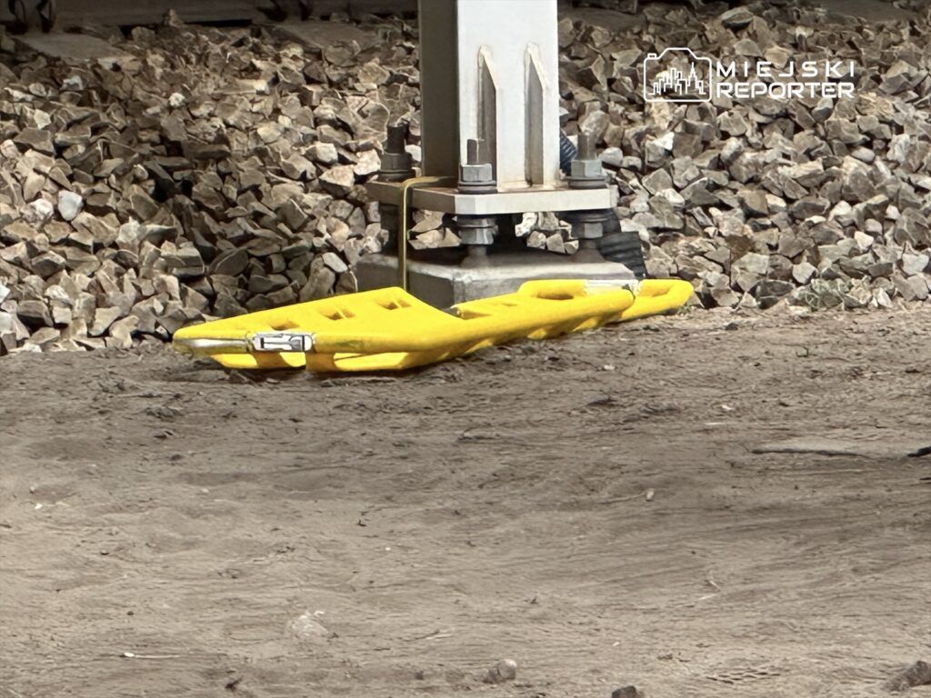 Żółta deska ratunkowa leży na ziemi obok fundamentu, w otoczeniu kamieni i ziemi.