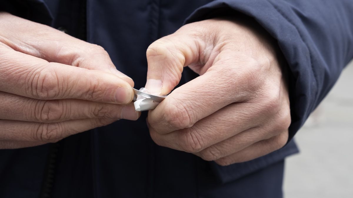 man on the street about to take a pill
closeup of a caucasian man on the street, wearing a blue parka, getting a pill from a blister pack
nito100