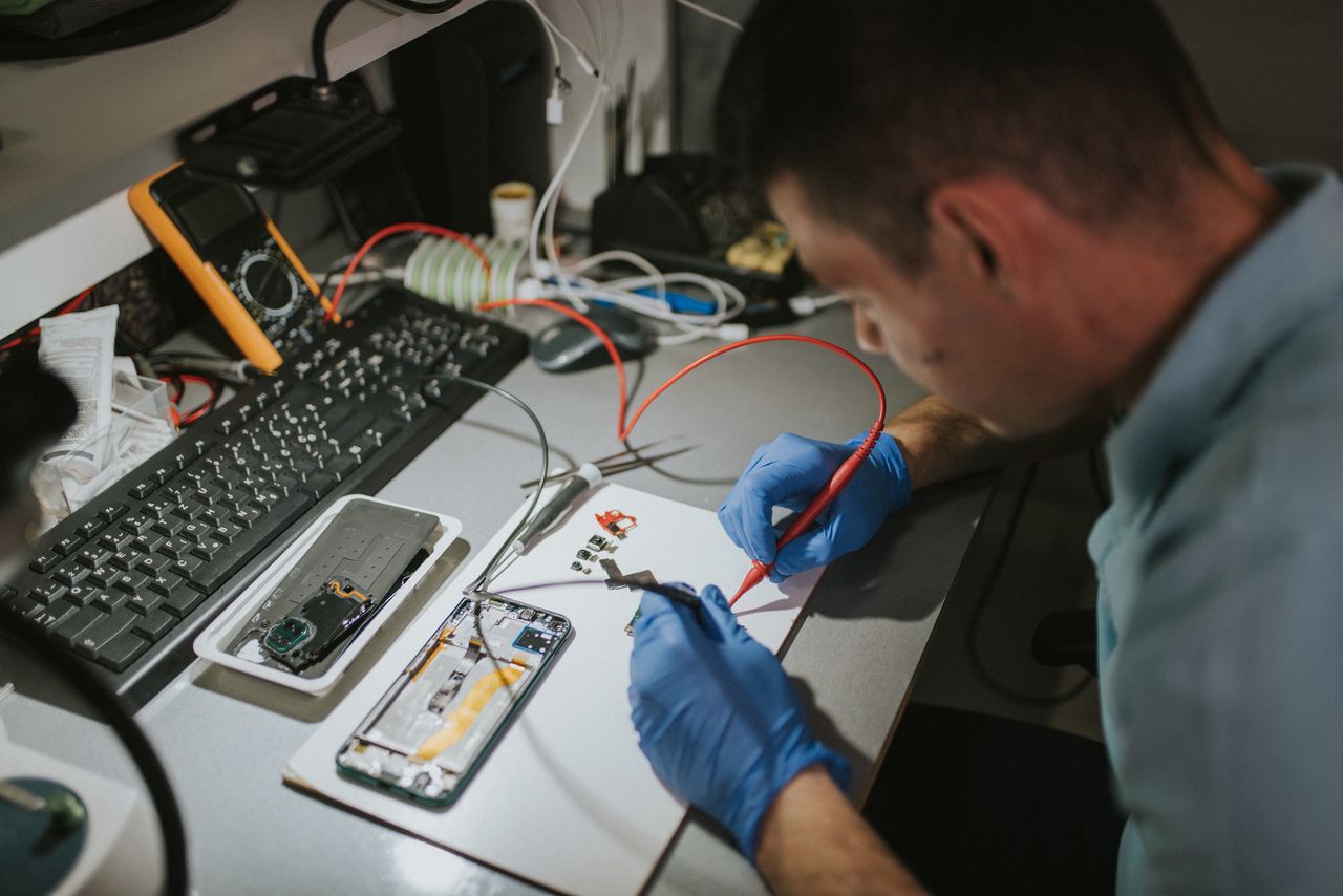 Technician checking broken smartphone at table in repair shop, closeup