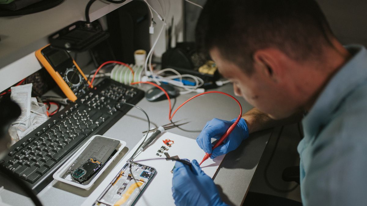 Technician checking broken smartphone at table in repair shop, closeup