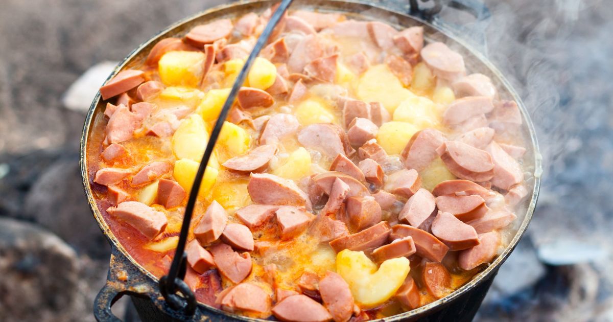 Kiełbasa i warzywa duszące się w żeliwnym kociołku nad ogniskiem