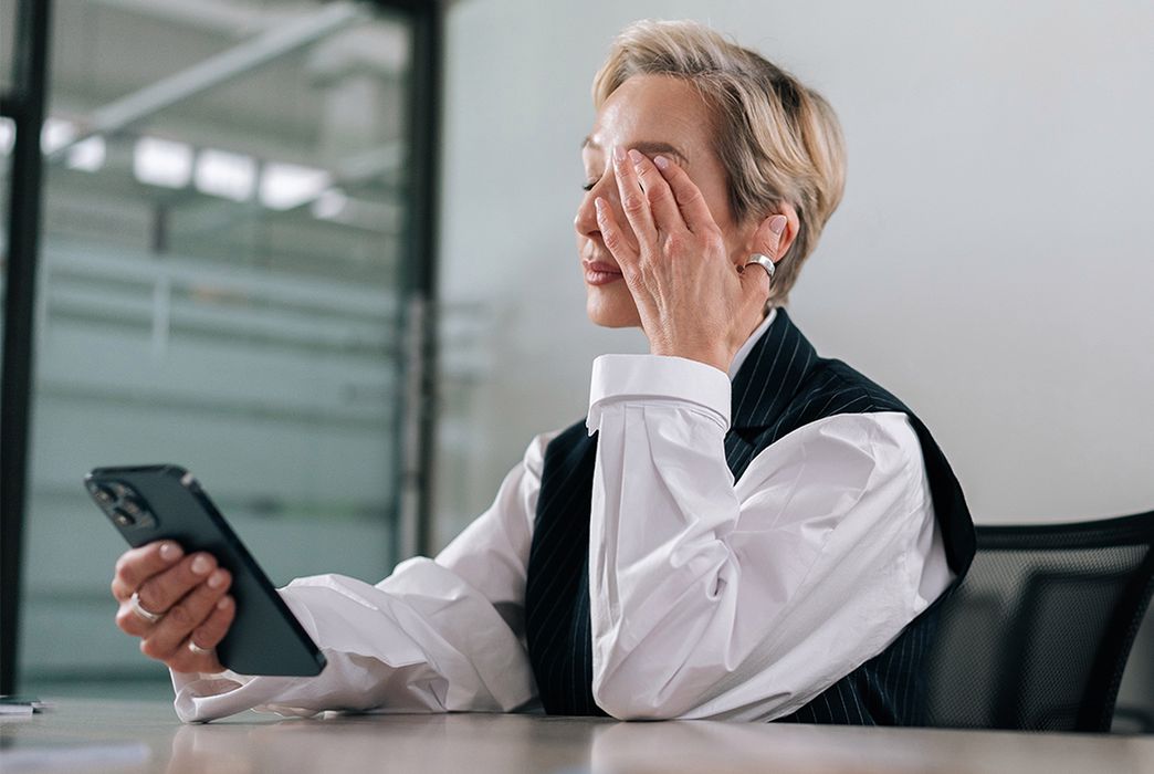 Kobieta używająca smartfona w salce konferencyjnej i przecierająca oczy ze zmęczenia i suchości oka - zdjęcie