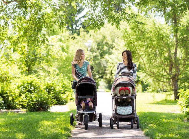 Matki spacerują z dziećmi w wózkach po parku. 