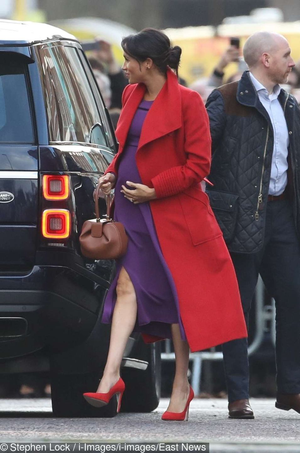 Meghan Markle z ciążowym brzuszkiem w czerwonym płaszczu