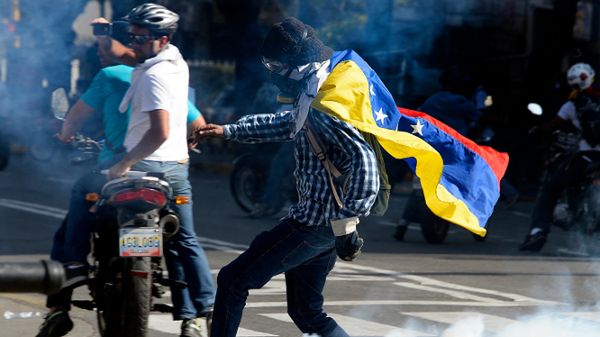 Uczestnik manifestacji próbuje kopnąć pojemnik z gazem łzawiącym