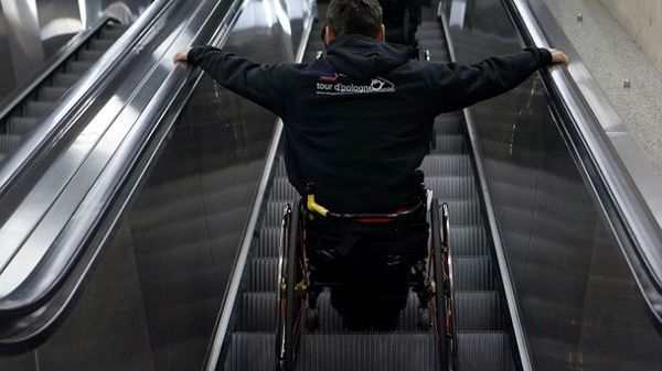 Mężczyzna na wózku inwalidzkim pokonuje schody ruchome na dworcu kolejowym