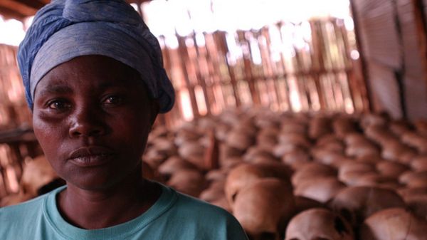 Kobieta ocalała z ludobójstwa na tle czaszek ofiar przy kościele Ntarama
