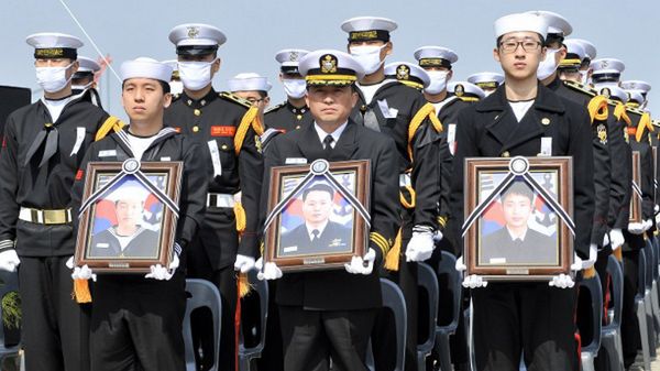 Ocaleli marynarze trzymają portrety ofiar podczas uroczystości pogrzebowych w 2010 r.
