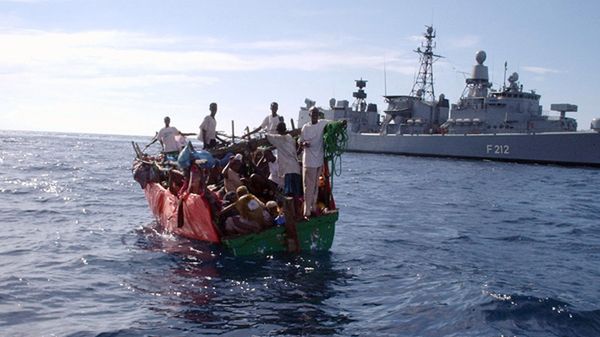 Przepełniona łódź z somalijskimi imigrantami. W tle niemiecka fregata FGS Karlsruhe
