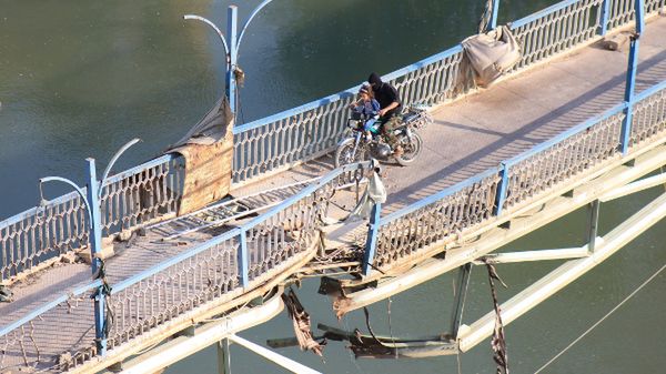 Mężczyzna z dzieckiem próbuje przedostać się przez zniszczony podczas wojny most, Deir Ezzor