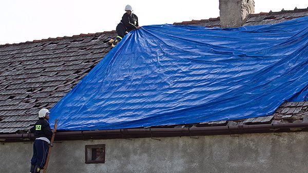 Strażacy zabezpieczają płachtą dach zniszczony przez grad
