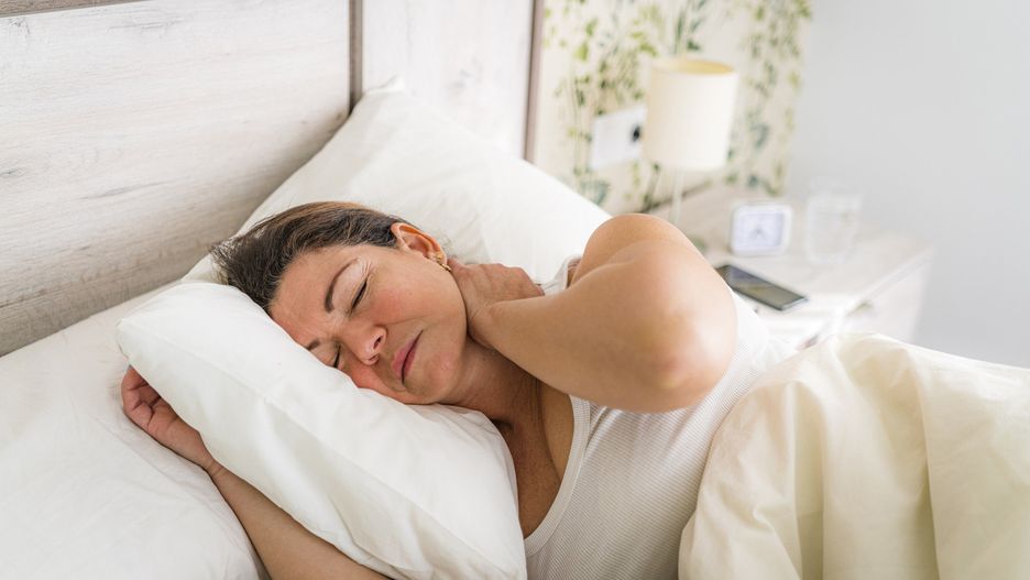 Portrait of a woman laying in bed touching her painful neck