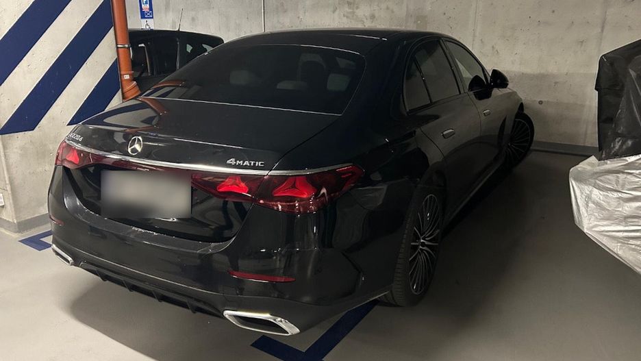 Czarny samochód marki Mercedes zaparkowany w podziemnym garażu z szarymi ścianami i oznaczeniami.