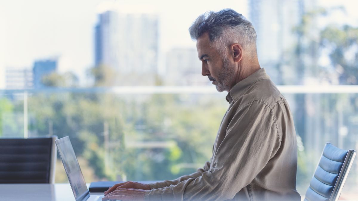 Businessman using a laptop computer. There is a large office window with a view in the background. Copy space