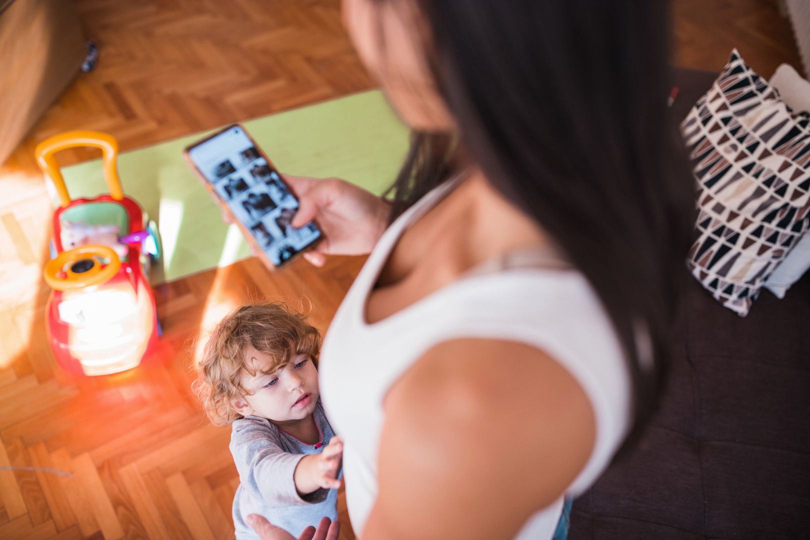 Toddler approaching woman looking at photo gallery on mobile phone
Mother using smart phone and toddler wanting to be held
Dobrila Vignjevic