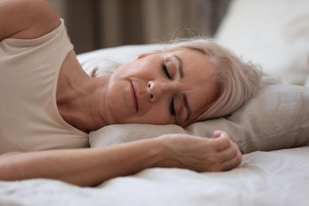 Calm healthy mature older woman lying on comfortable pillow orthopedic mattress sleeping well in cozy bed, serene middle aged lady beautiful face enjoy peaceful sleep relax at home, close up view