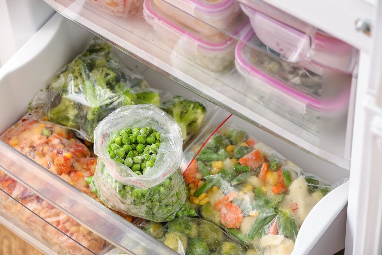 Plastic bags with frozen green peas and different vegetables in refrigerator