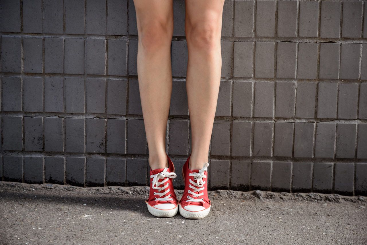 Close up photo of girl's legs in red keds standing over grey wall. Copy space.