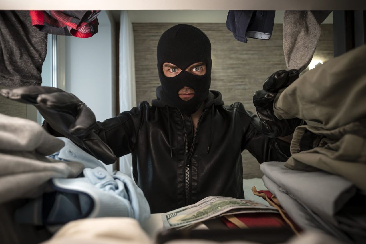 a thief in a black mask searches a wardrobe in search of money and valuables. concept of apartment theft. stealing clothes.