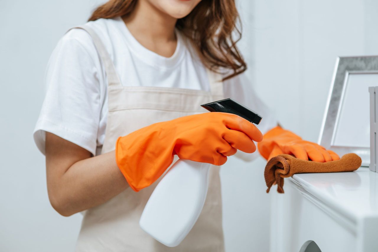 Close up hand of young housekeeper woman in rubber gloves use cleaning solution in a spray bottle on white furniture and Use a cloth to clean it. copy space