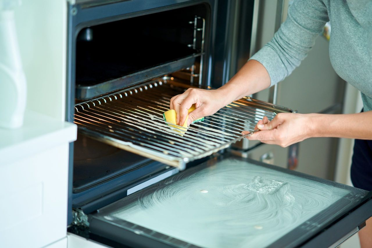 Young woman cleaning oven in the kitchen. High quality photo