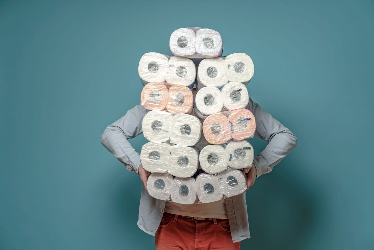 Man in a medical mask, in a panic, stocked up with toilet paper, he fears quarantine during a virus outbreak. Isolated on a blue background. Concept of paranoia.