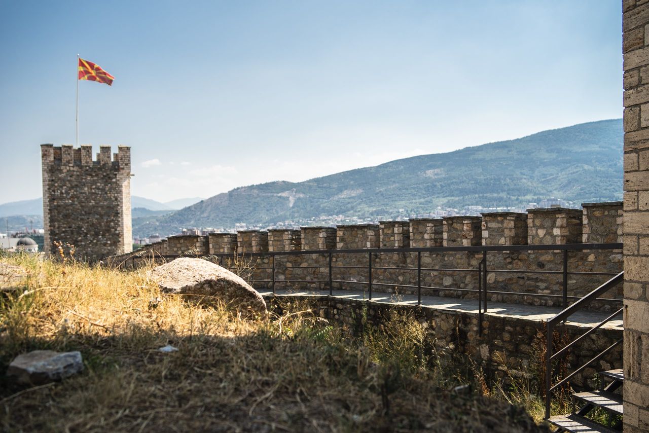 An old castle with the flag of Macedonia on it surrounded by hills covered in greenery