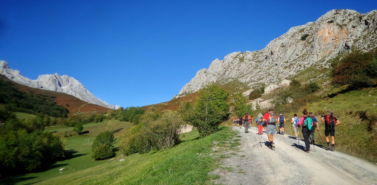 The hikers walking through a pathway surrounded by hills covered in greenery under the sunlight at daytime