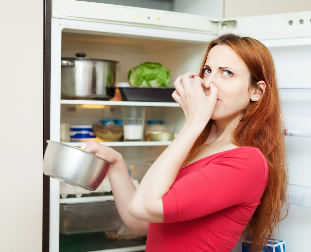 woman in red holding foul food near   refrigerator