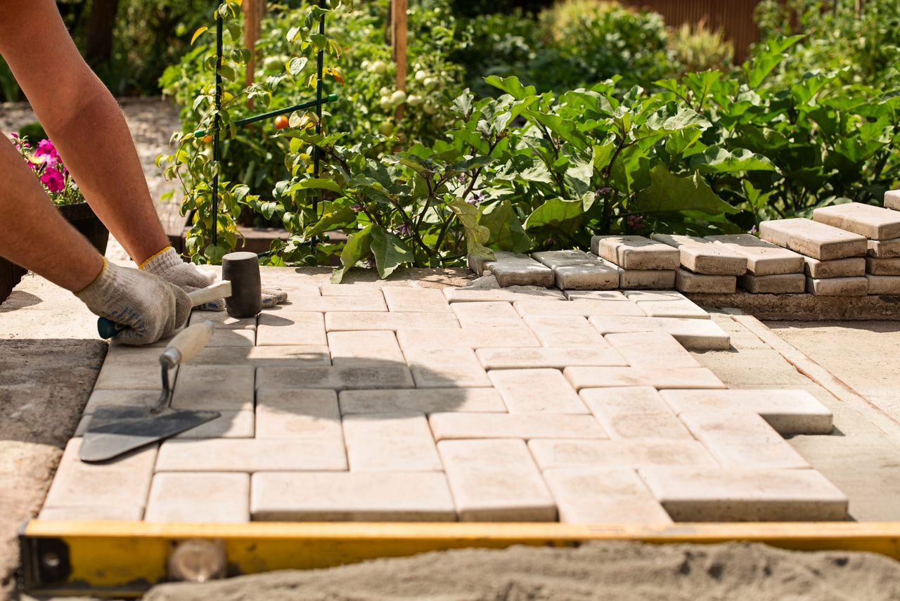 The master  lays paving stones in layers. Garden brick pathway paving by professional paver worker. Laying gray concrete paving slabs in house courtyard on sand foundation base.