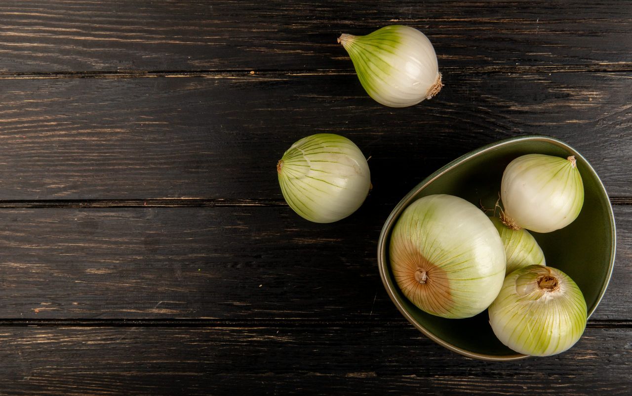 top view of white onions in bowl on wooden background with copy space